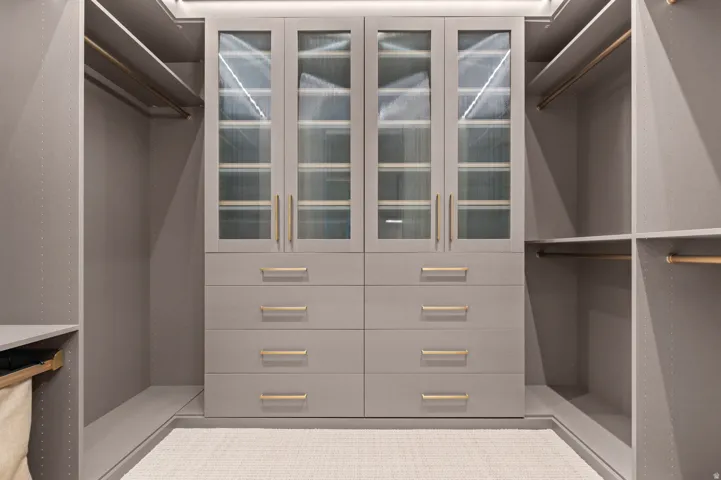 Custom closet system featuring built-in cabinetry, glass-front upper cabinets, integrated drawers with gold-tone hardware, and multiple clothing rods