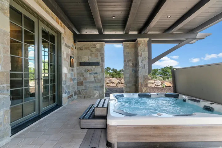 Covered patio with a built-in spa, stone exterior, French doors, and wood-beam ceiling