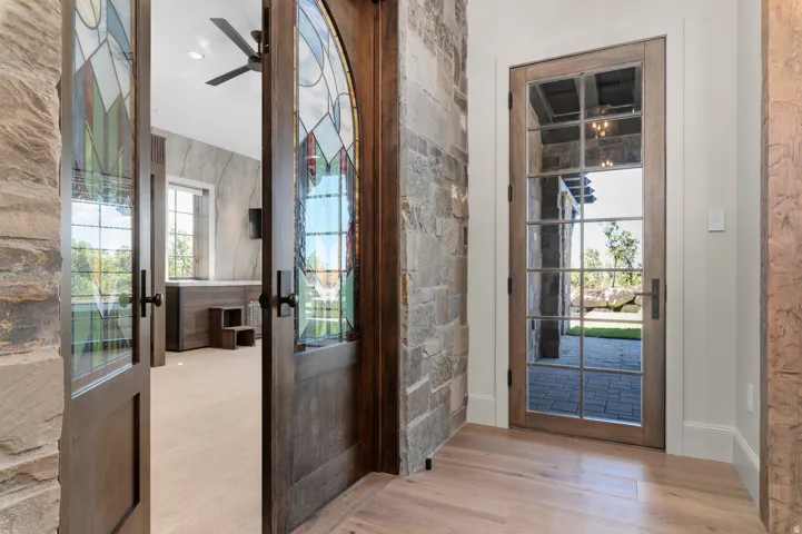 Stained glass double doors, stone wall accents, light wood-finish flooring, and a glass-paned exterior door
