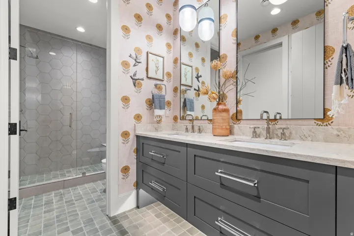 Dual vanity with a light-toned countertop, custom dark cabinetry, and two large mirrors