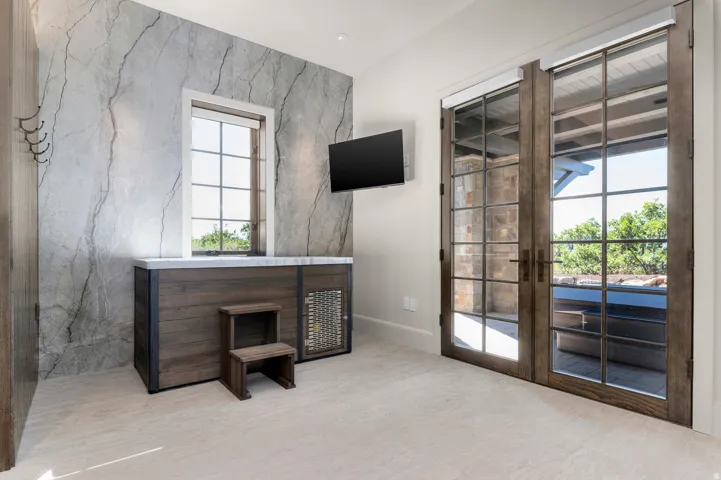 Wood-finish double doors with divided lites, natural stone accent wall, built-in wood-finish cabinetry, and light-toned carpet flooring