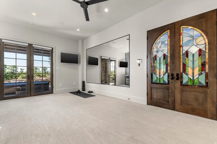 Double stained-wood doors with intricate stained-glass panels, expansive full-length mirror, wood-framed glass double doors, modern ceiling fan, and recessed lighting
