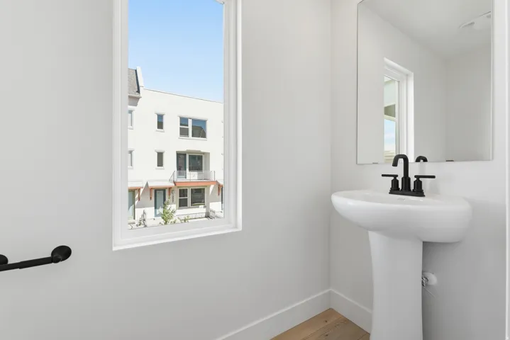 Pedestal sink with a matte black faucet, wall-mounted mirror, and wood-finish flooring