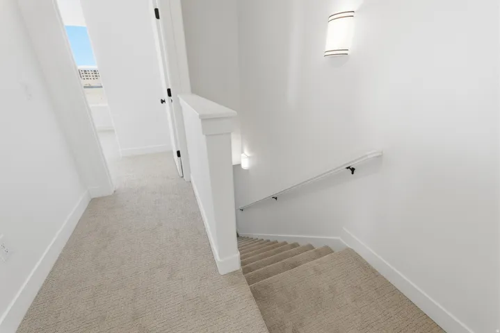 Carpeted hallway with white walls, white railing, and a wall-mounted light fixture