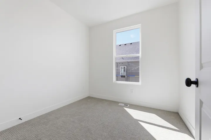 Carpeted flooring, white walls, white trim, single window, white paneled door with black hardware