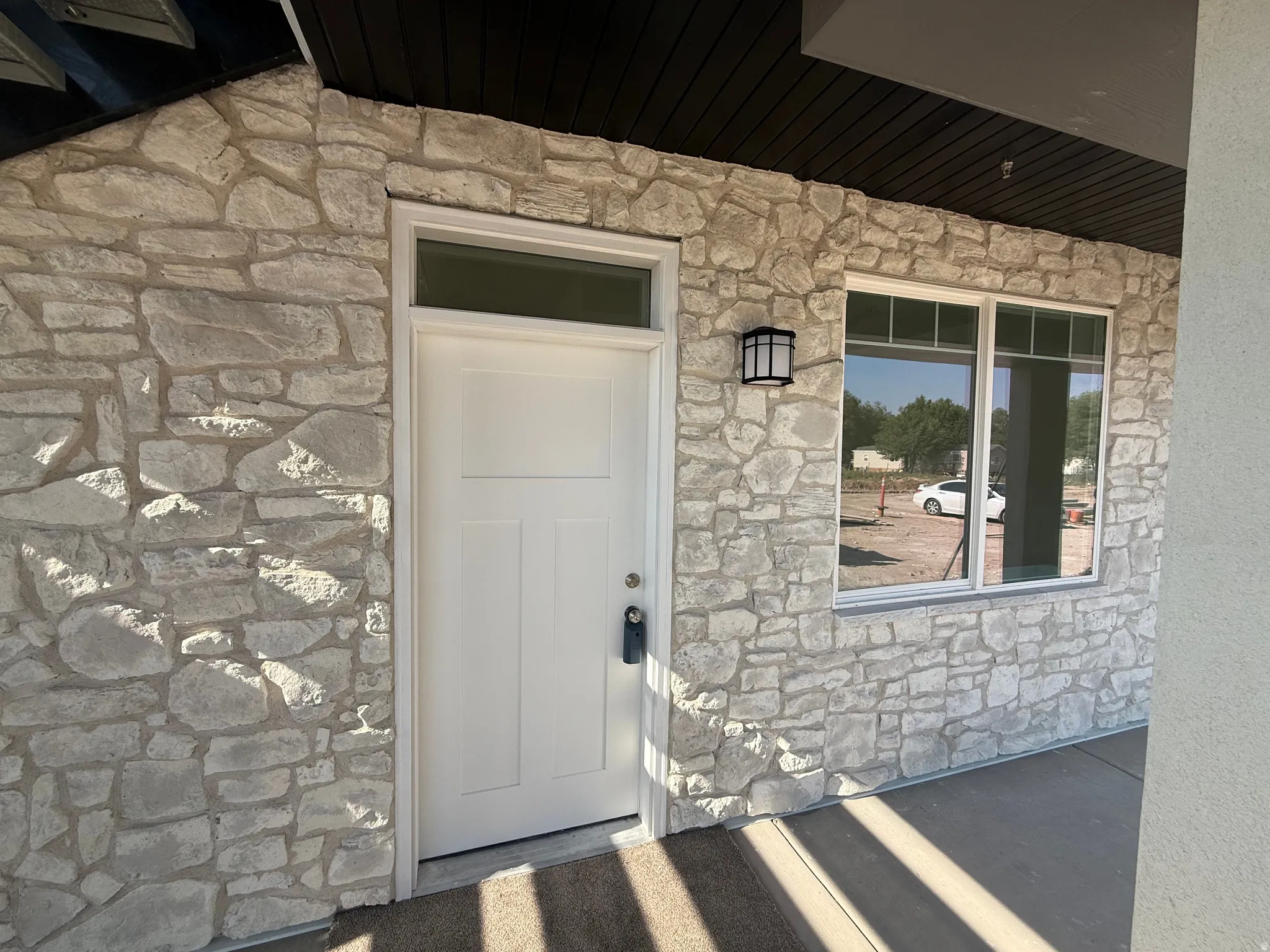 Stone veneer exterior, white paneled entry door with transom window, exterior wall lantern, and multi-pane window