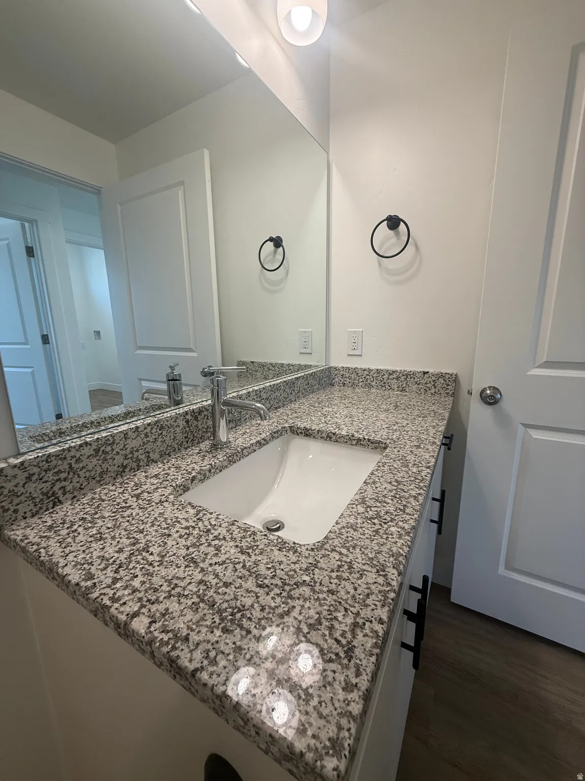 Granite-finish countertop with an undermount sink, chrome faucet, white vanity with matte black hardware, and a large wall-mounted mirror