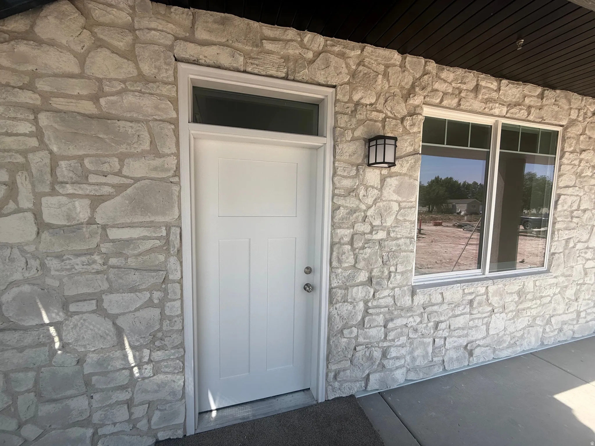Stone veneer exterior with a white entry door, transom window, and a wall-mounted light fixture