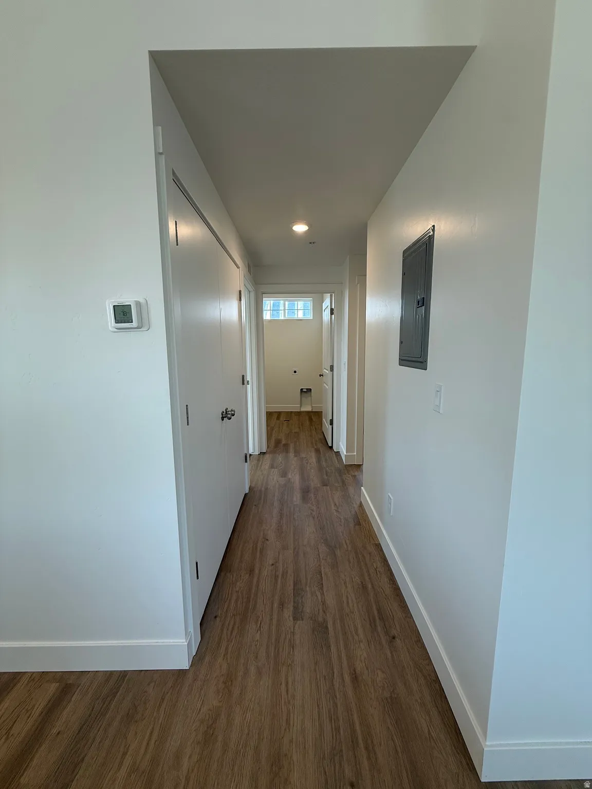 Modern hallway featuring wood-finish flooring, recessed ceiling lighting, and clean white walls with multiple doorways providing access to adjoining spaces