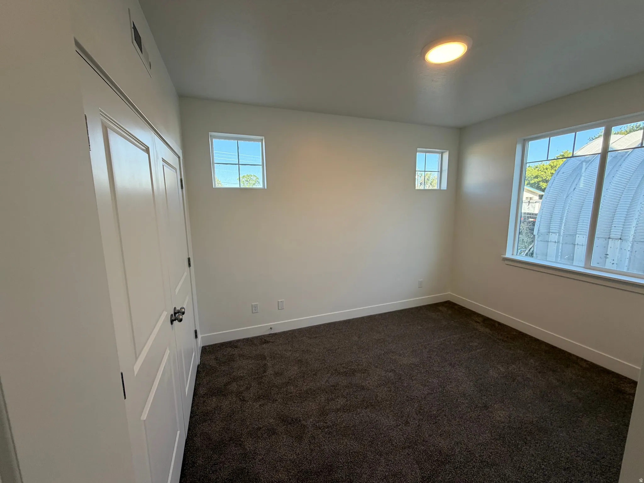 Neutral tone wall finishes, dark textured carpeting, two paneled doors with black hardware, and multiple windows