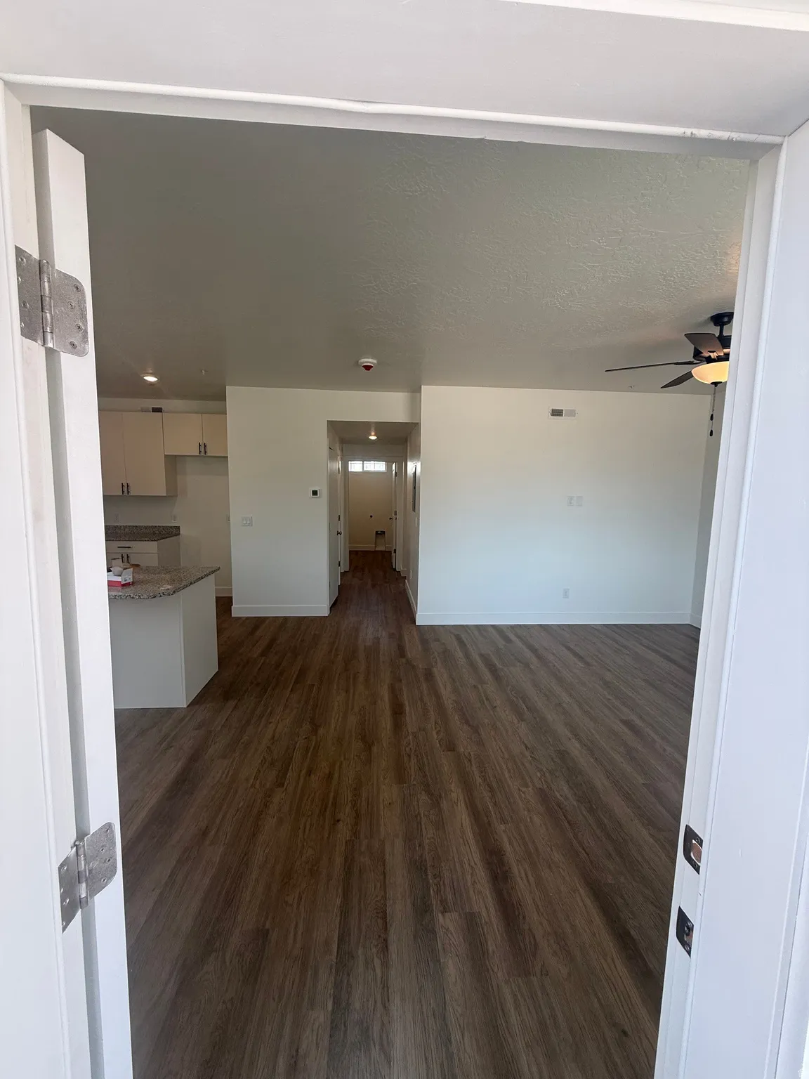 Wood-finish flooring throughout, recessed lighting, ceiling fan, white cabinetry, and a kitchen island with a stone countertop