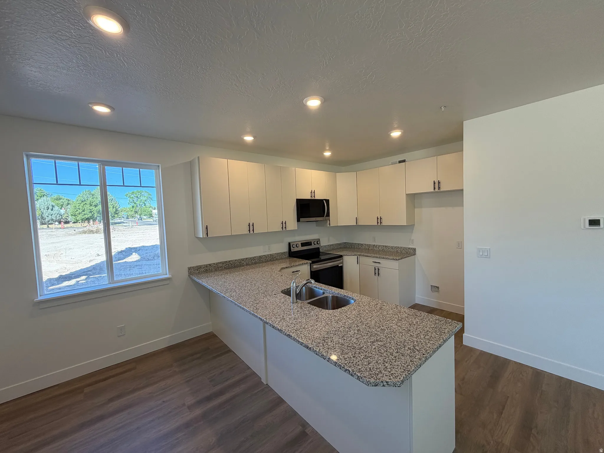 Kitchen featuring a large island with dual sinks, white cabinetry with dark hardware, speckled countertops, and wood-finish flooring