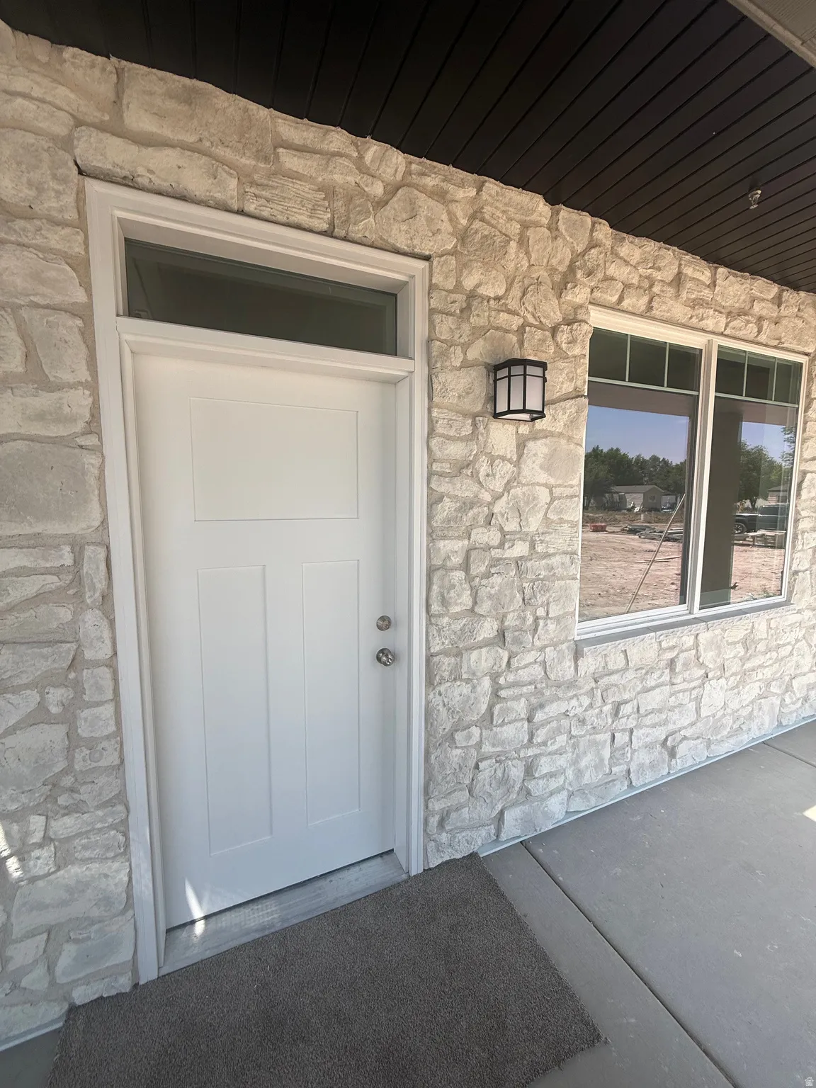 Stone facade featuring white trim, a transom window above the entry door, and a black exterior light fixture