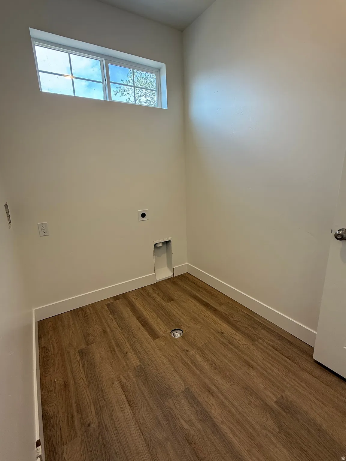 Wood-finish flooring with white baseboards, a high-set transom window, and dedicated appliance hookups