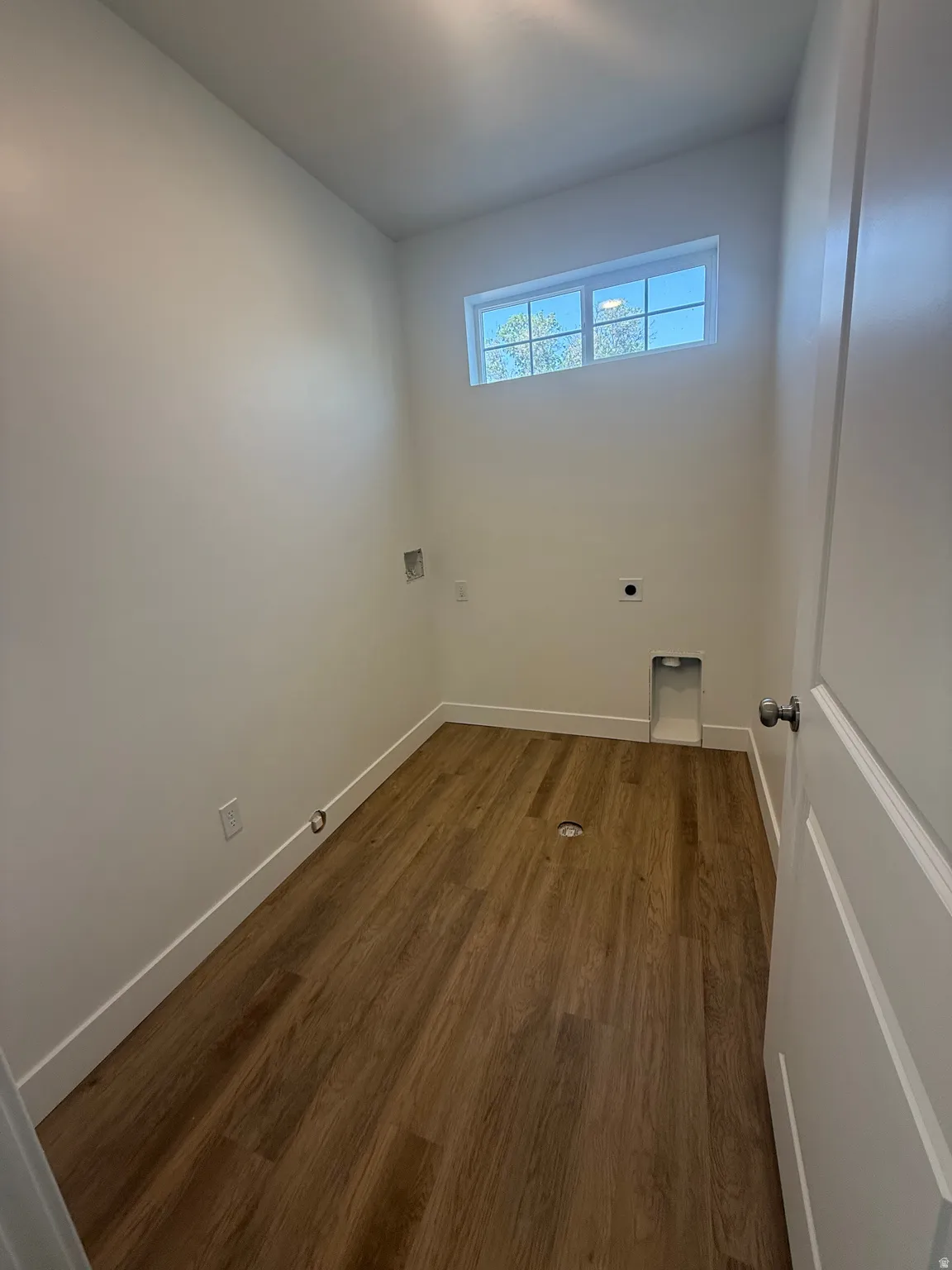 Laundry area featuring wood-finish flooring, a transom window, and white trim