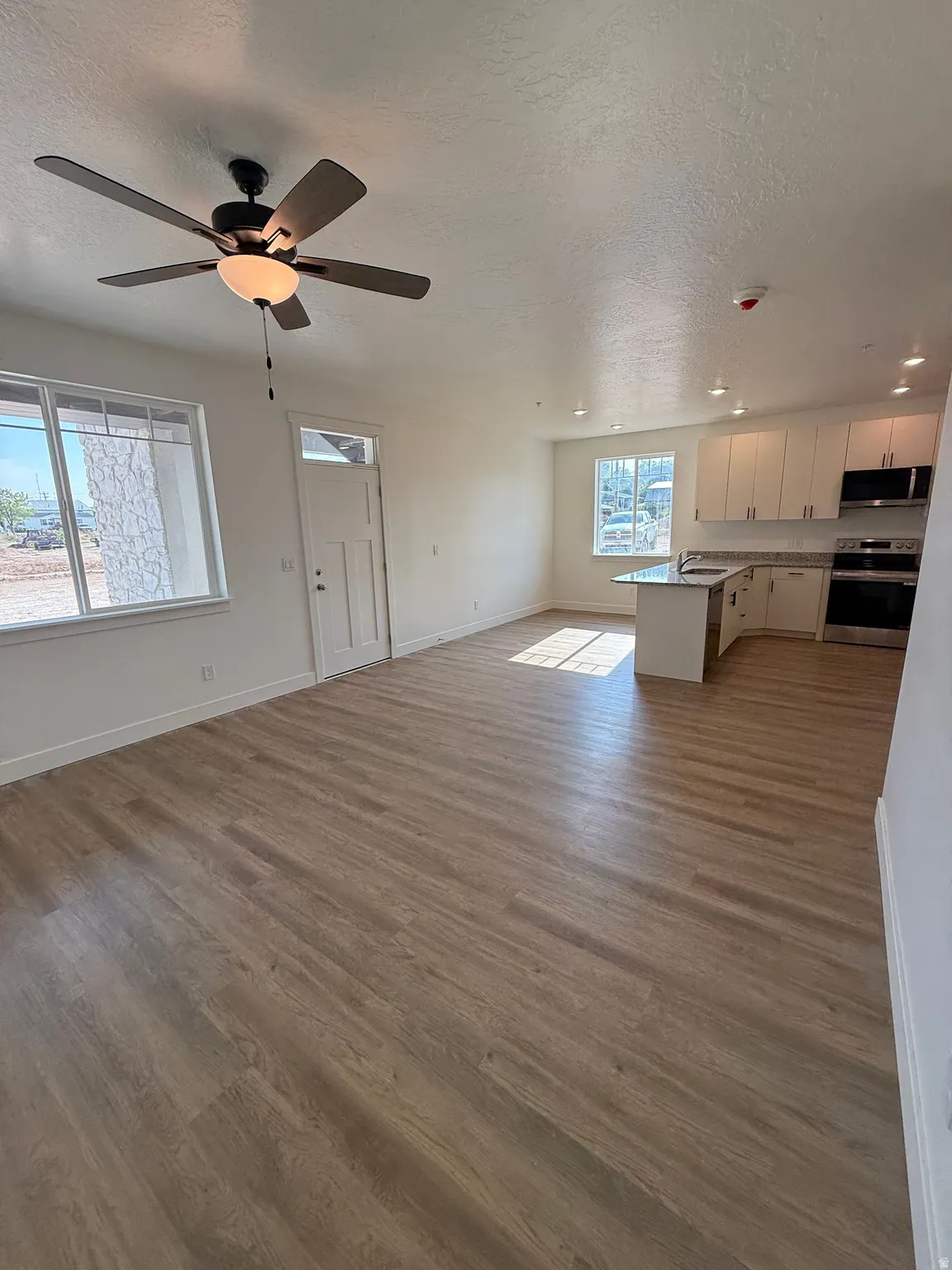 Open-concept living space featuring wood-finish flooring, a ceiling fan with integrated lighting, recessed lighting, and a kitchen with stainless steel appliances