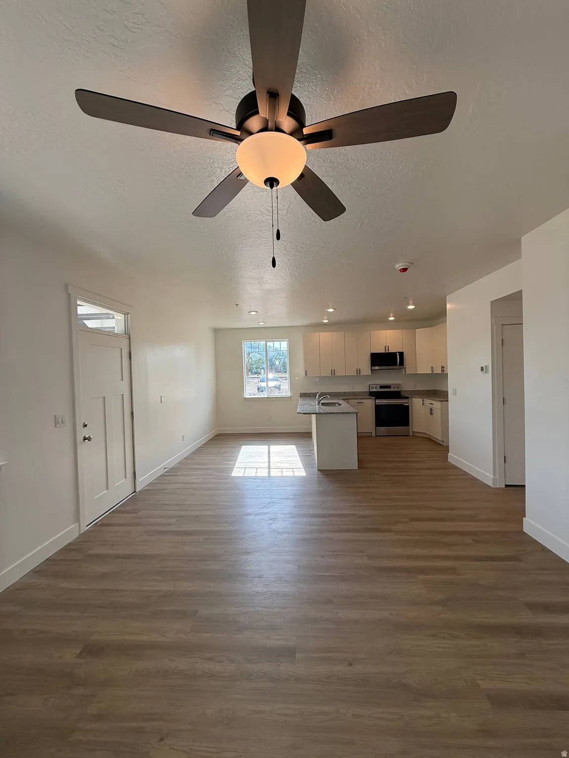 Open-concept living space featuring wood-finish flooring, a ceiling fan with integrated lighting, recessed lighting, white cabinetry, and light-toned countertops