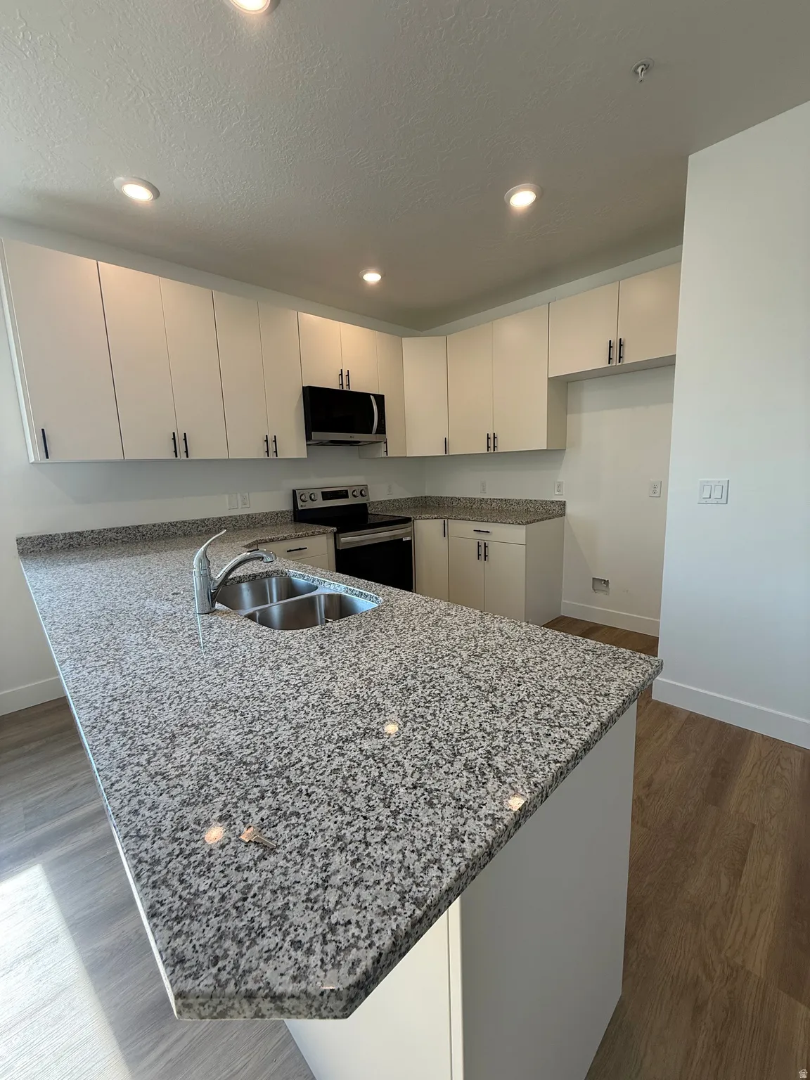 Kitchen featuring white cabinetry, granite countertops, stainless steel appliances, and wood-finish flooring
