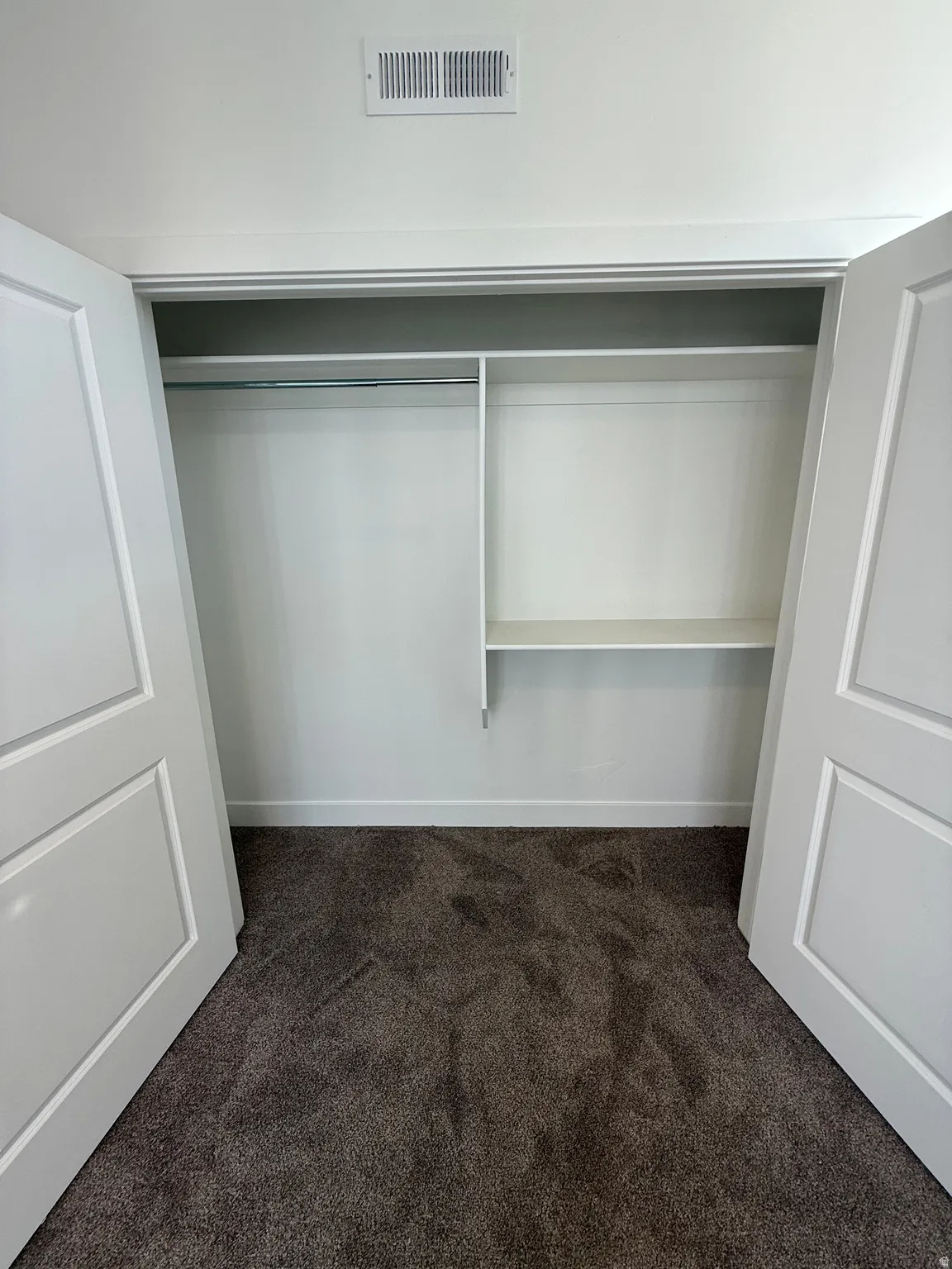 Double-door closet featuring a hanging rod, integrated shelving, and dark-toned carpeting