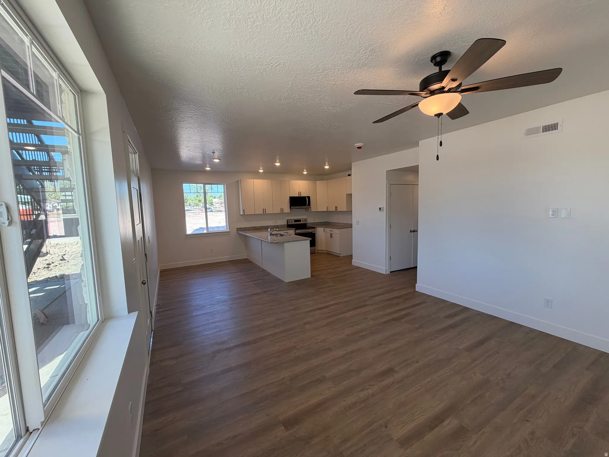Wood-finish flooring throughout, with a ceiling fan featuring integrated lighting, a kitchen with white cabinetry, and recessed lighting