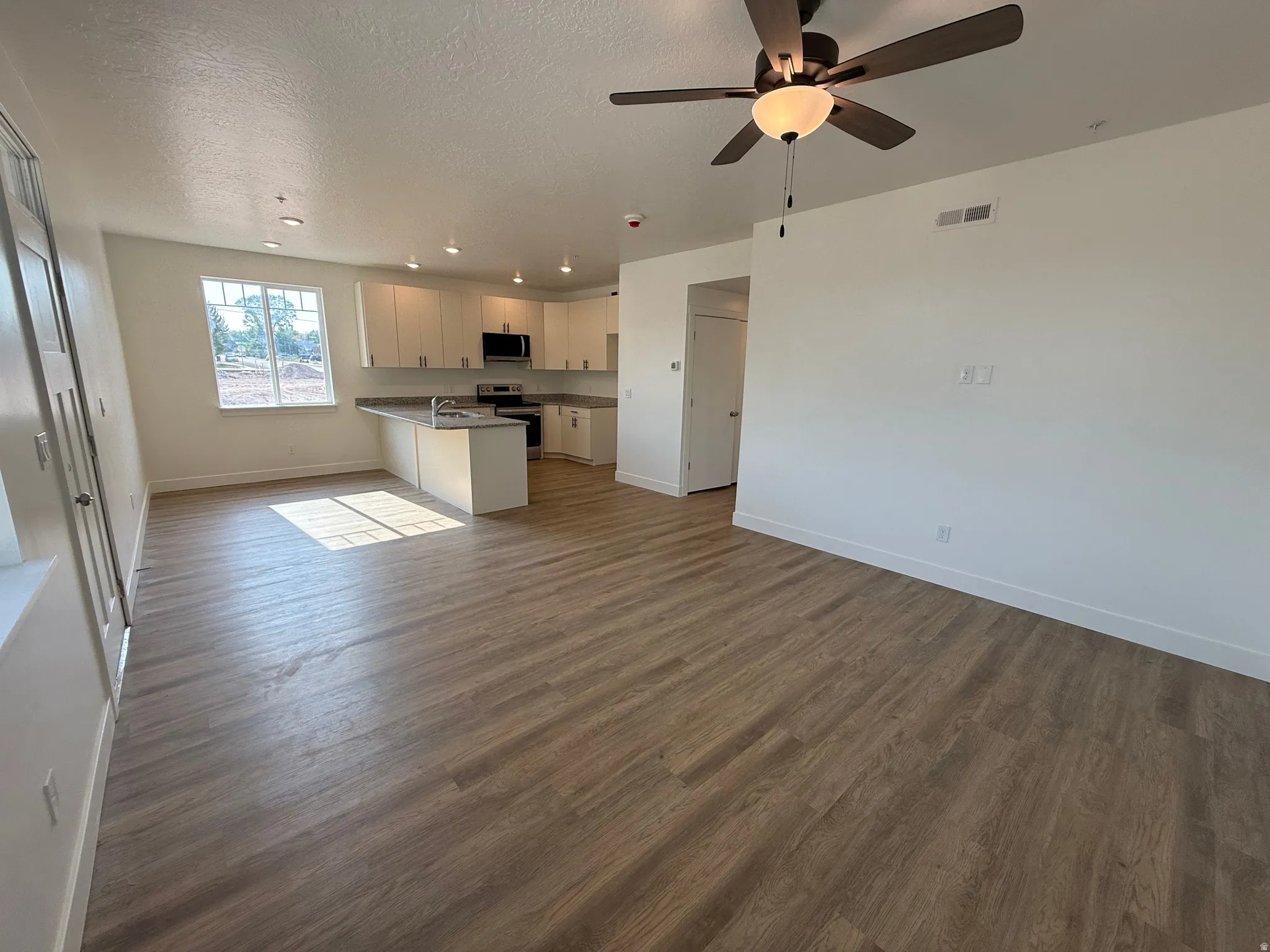 Open-concept living space with wood-finish flooring, recessed lighting, and a ceiling fan