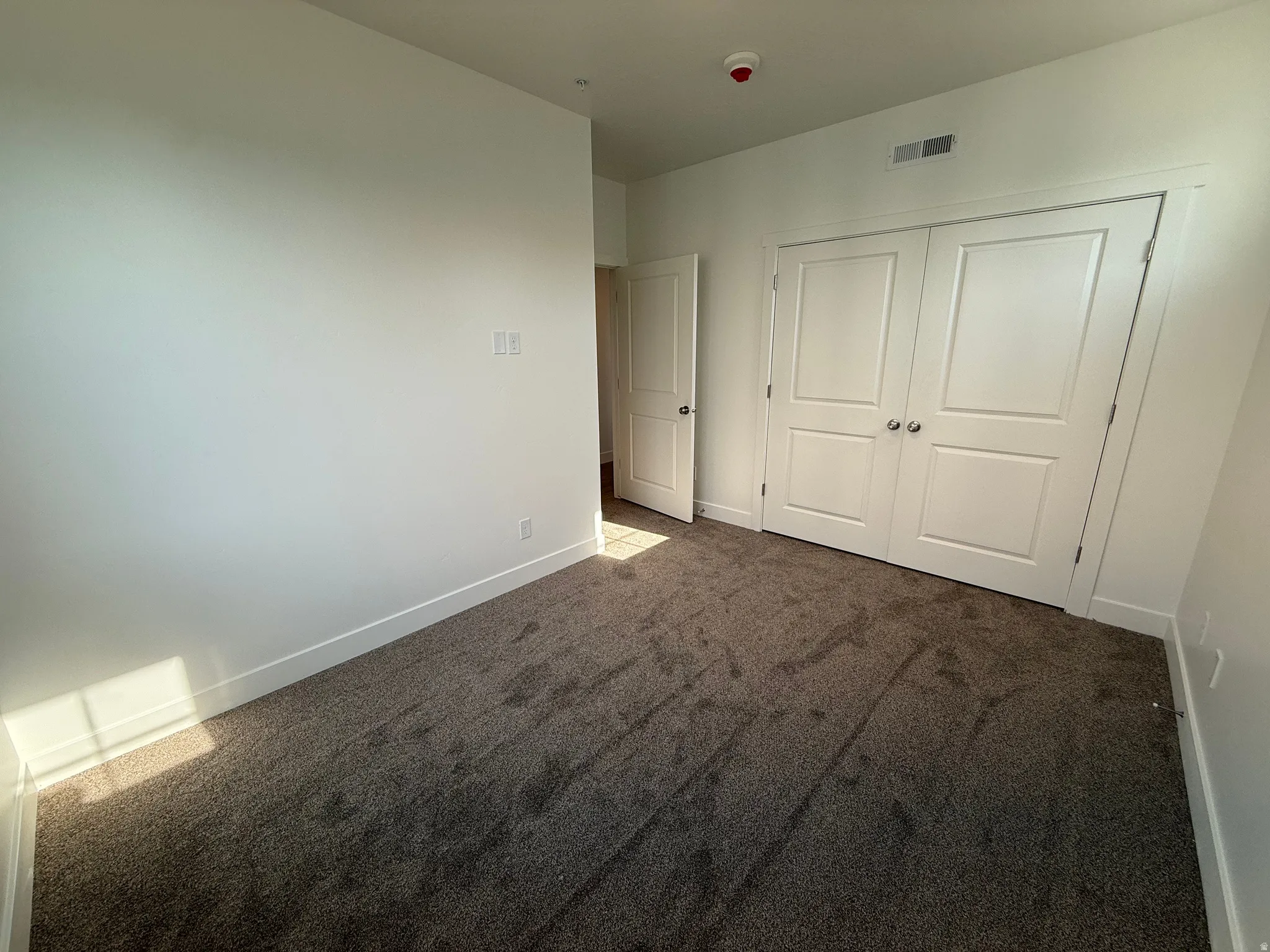 Neutral wall color with white trim, featuring carpet flooring, bifold doors, and a recessed light fixture