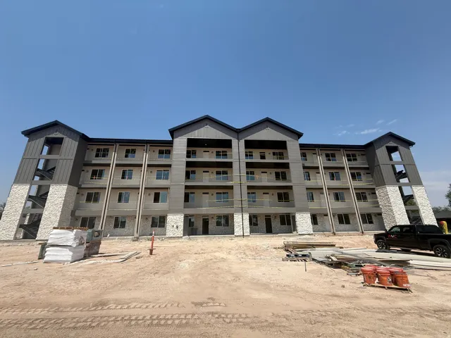 Multi-story residential building featuring a stone and siding exterior, multiple balconies with railings, and large windows