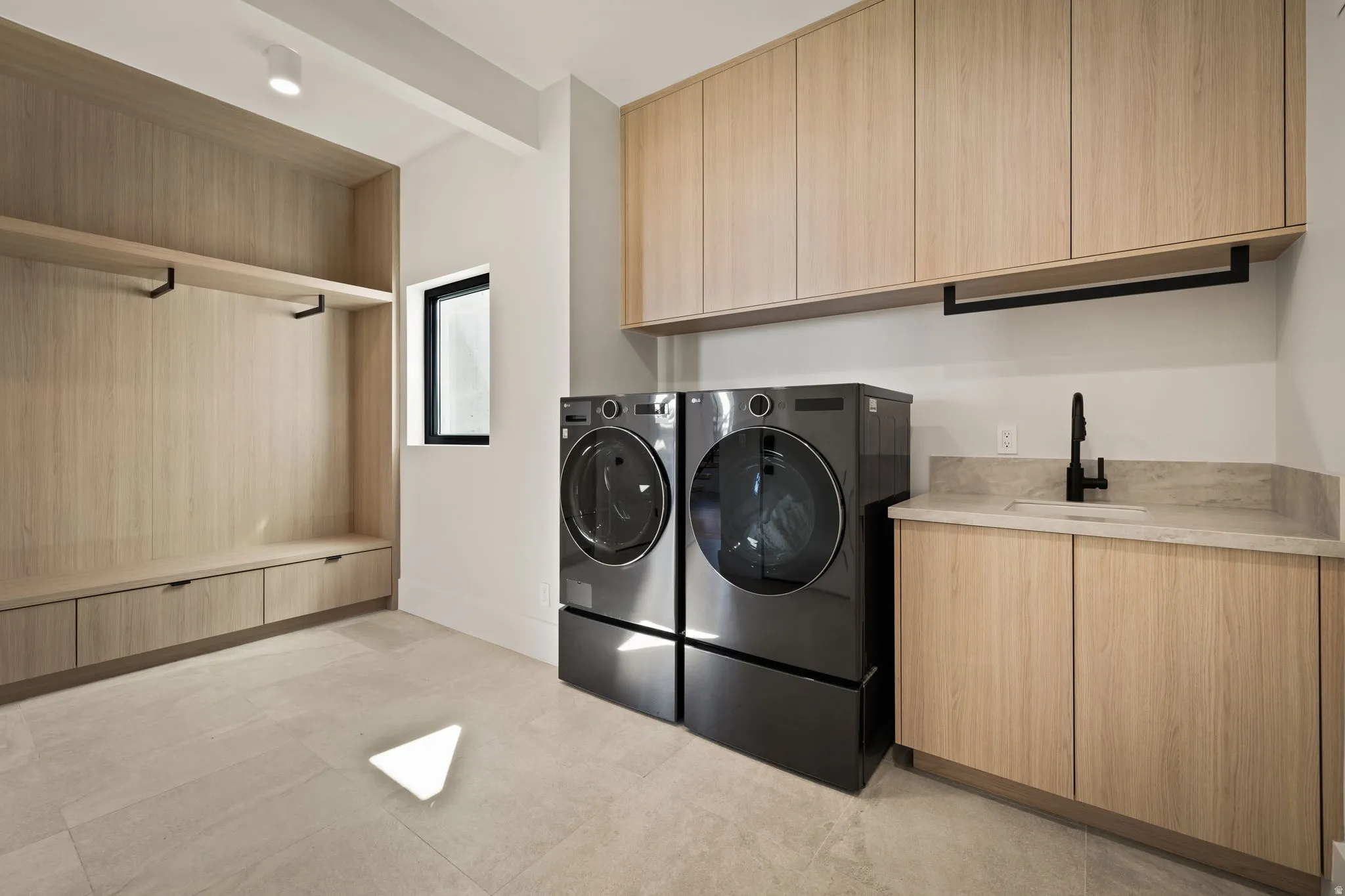 Built-in wood-finish cabinetry, light-toned flooring, undermount sink with a matte black faucet, and a black-framed window