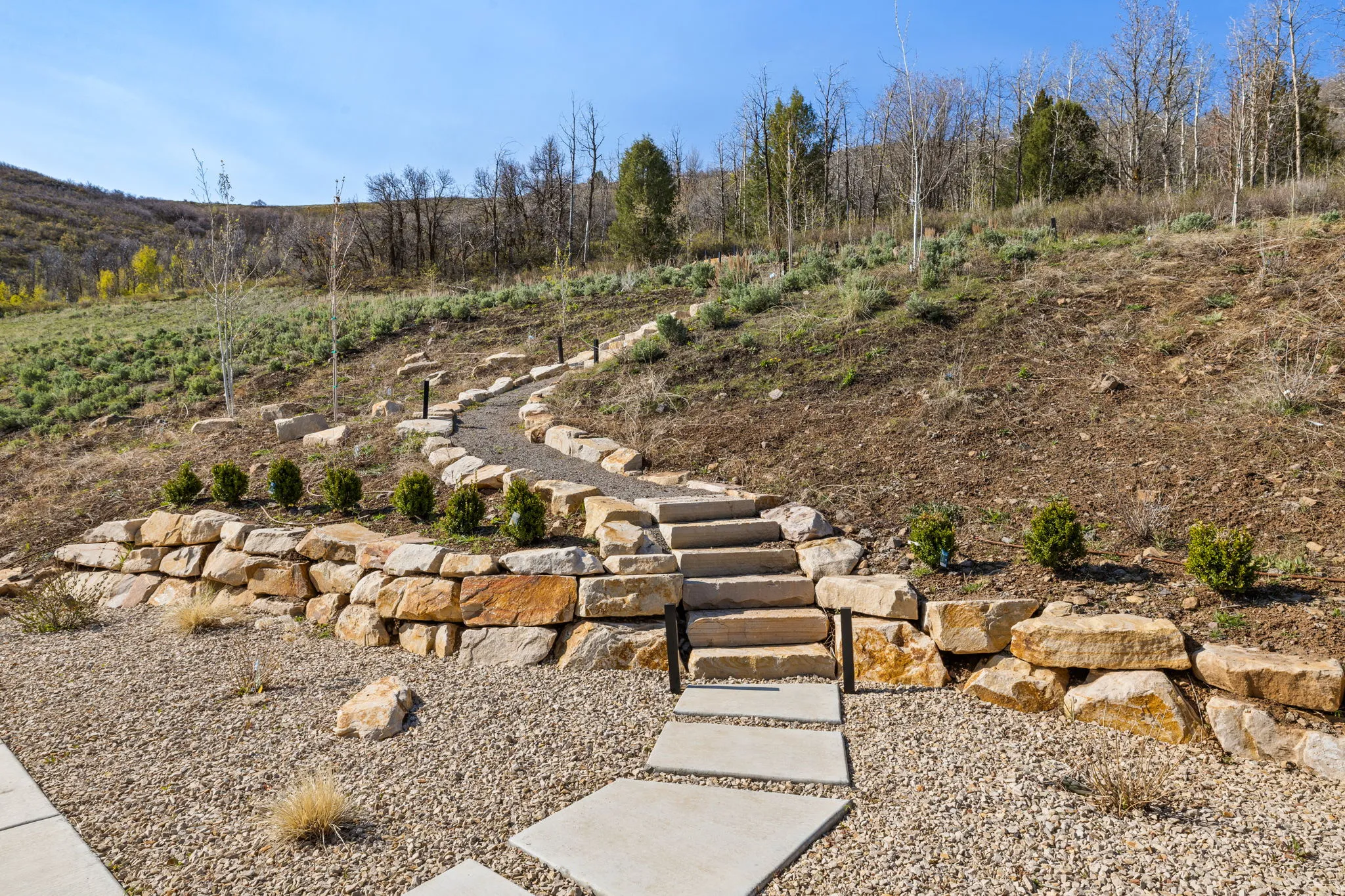 Terraced landscaping featuring a stone retaining wall, concrete stepping stones, and a gravel pathway