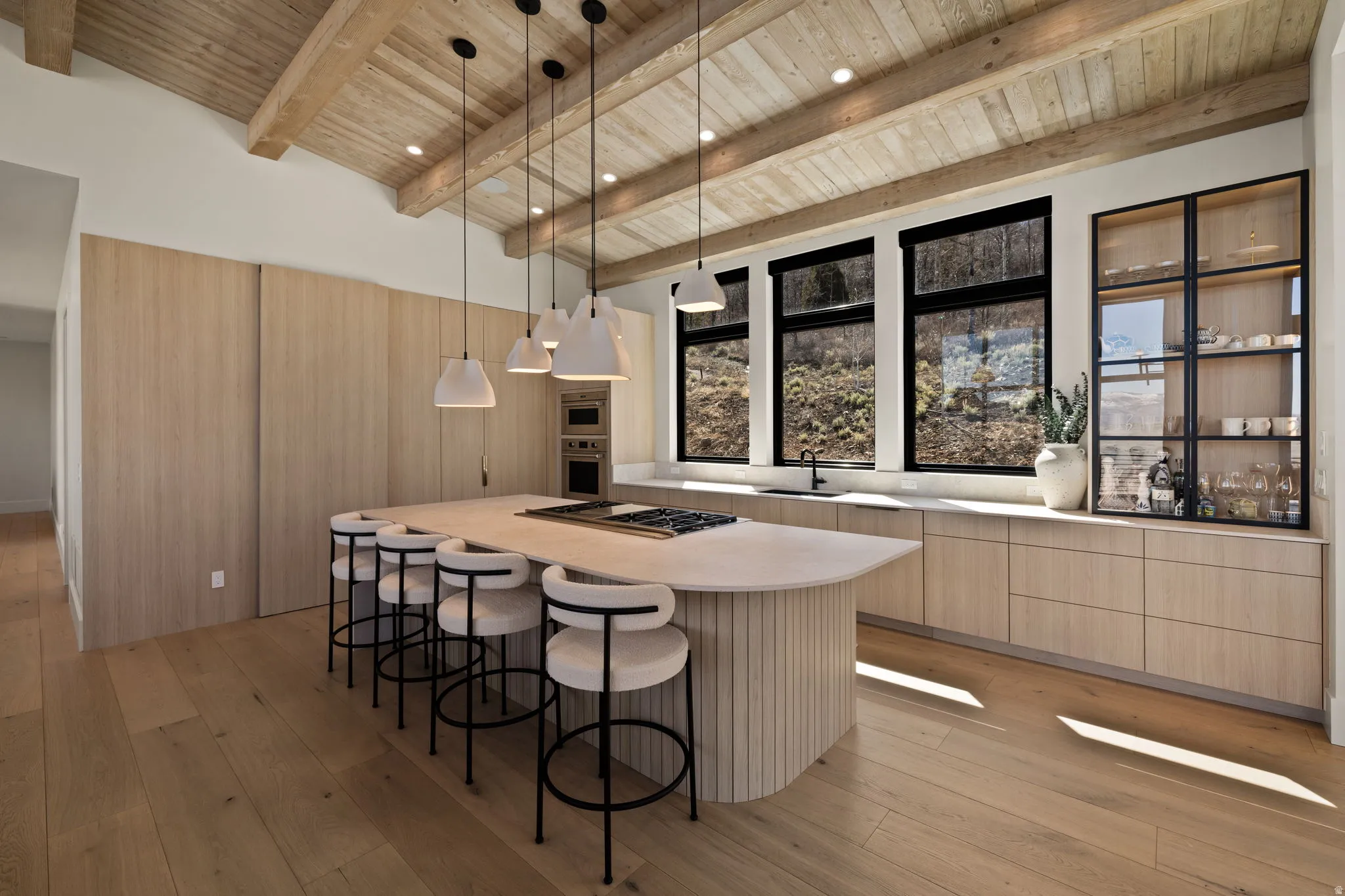 Vaulted wood-beamed ceiling, wood-finish flooring, custom wood cabinetry, integrated stainless steel appliances, and a large central island with pendant lighting