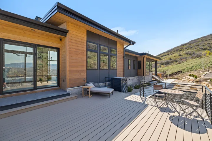 Expansive outdoor deck with composite decking, modern cable railings, multiple sliding glass doors, and natural wood siding