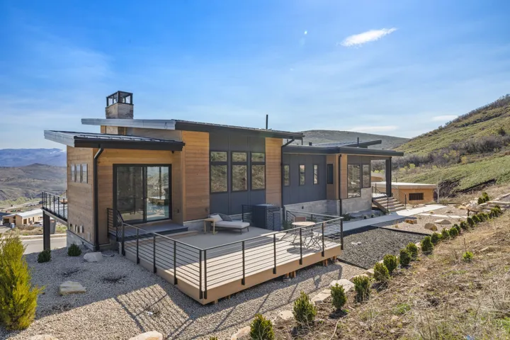 Contemporary exterior featuring wood siding, a flat roofline, an expansive deck with metal railings, and a gravel landscape