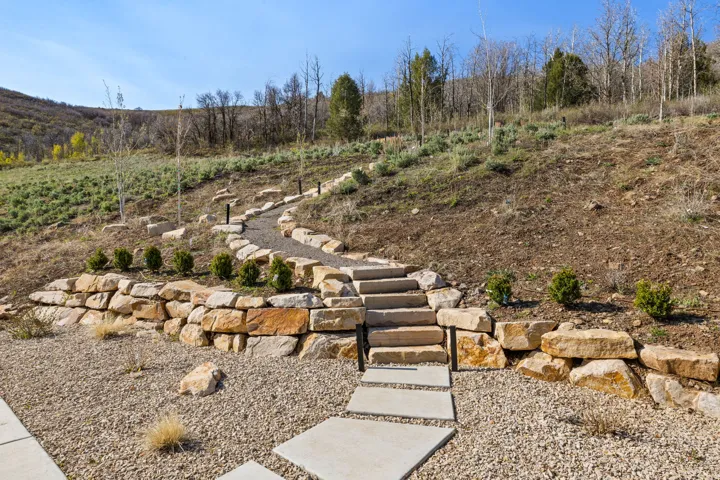 Terraced landscaping featuring a stone retaining wall, concrete stepping stones, and a gravel pathway