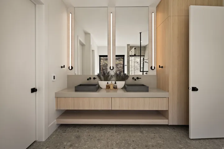 Floating wood-finish vanity with dual vessel sinks, wall-mounted matte black faucets, and integrated lighting