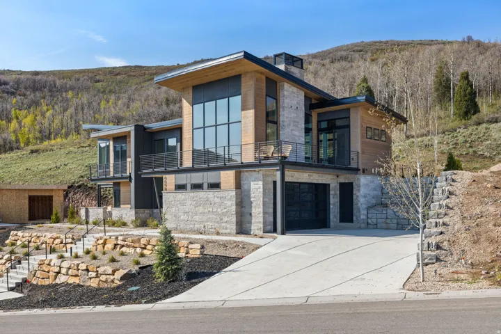 Contemporary exterior with wood siding, expansive multi-story windows, stone-clad lower level, integrated balcony, and a multi-level driveway