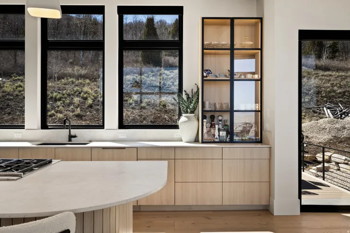 Blonde wood-finish cabinetry, light-toned countertops, integrated sink with matte black faucet, and a built-in display cabinet with glass doors