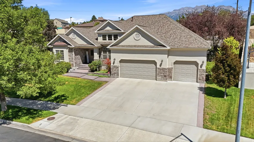Stucco and stone exterior with a multi-car garage, concrete driveway, and front lawn
