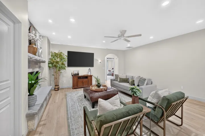 Recessed lighting illuminating wood-finish flooring, a stone-clad fireplace, and an arched doorway
