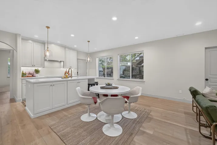 Open-concept kitchen with white shaker cabinetry, an island with seating, a gold-finish faucet, and wood-finish flooring