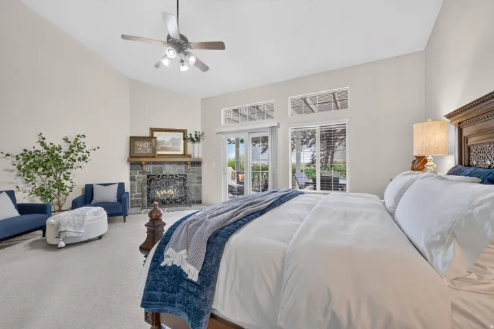 Spacious primary bedroom suite featuring a fireplace with stone surround, dual beds, ceiling fan with integrated lighting, expansive glass doors opening to outdoor space, and carpet flooring throughout