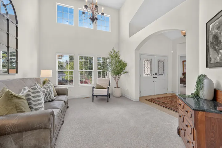 Vaulted ceilings with a chandelier, arched entryway, double front doors with decorative glass, and multiple windows