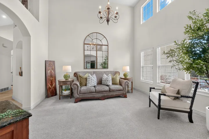 Voluminous ceiling height, arched architectural details, upper-level windows, light-tone carpeting, and a decorative chandelier
