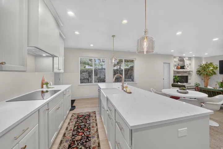 Modern kitchen featuring white cabinetry, light-toned countertops, a built-in cooktop, and a large center island with an undermount sink