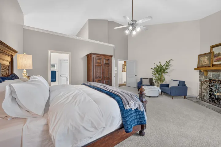 Spacious primary bedroom suite featuring vaulted ceilings, ceiling fan with integrated lighting, wood-finish flooring, and an attached ensuite
