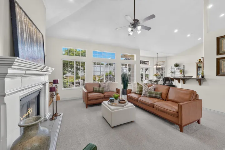 Vaulted ceiling with a ceiling fan, a fireplace with a white mantel, and multiple windows allowing natural light