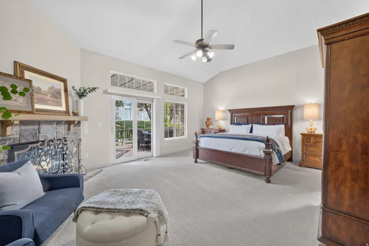 Vaulted ceiling with a ceiling fan, stone-faced fireplace, glass French doors, and transom windows