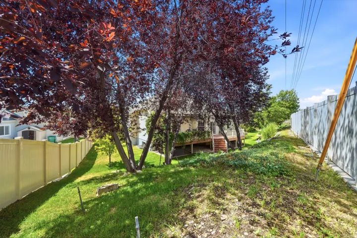 Sloped lawn with mature trees, a multi-level deck, and a privacy fence