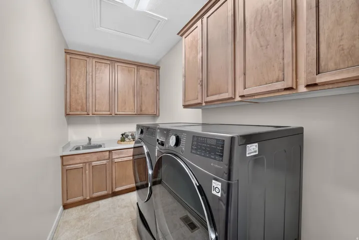Laundry room featuring a stainless steel sink, light wood-finish cabinetry, light-toned flooring, and a flat ceiling with an access panel