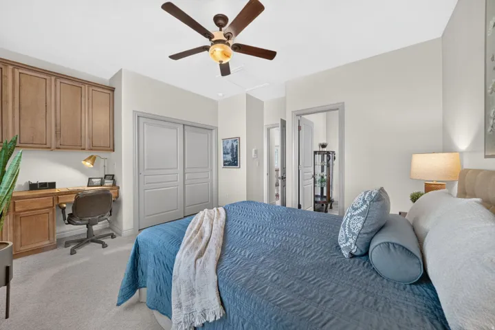 Integrated built-in desk with overhead cabinetry, ceiling fan with integrated lighting, and carpeted flooring