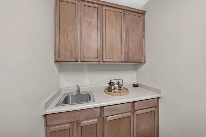 Wood-finish cabinetry with brushed nickel hardware, light-toned countertop, and stainless steel sink with chrome faucet